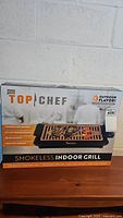 Closed top and front view of the Bravo Top Chef smokeless indoor grill box showing brand, product name, and features.