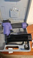 Purple and black Central Pneumatic air brad nailer in carrying case with accessories in a plastic bag.