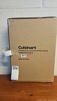 Photo of unopened cardboard box with printed label showing Cuisinart Carbon Steel Roaster with Rack, model CSR-1712RGR, made in China.