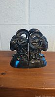 Pair of brass ram's head bookends placed side by side, showing front view of curled horns and facial details.