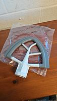 Photo of new KitchenAid Flex Edge Beater attachment in white with gray flexible edge on wooden surface.