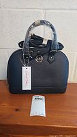Front view of Marilyn Monroe black dome top handbag, showing MM logo and handles wrapped in plastic