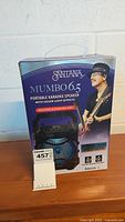 Front view of unopened Santana Mumbo 6.5 portable karaoke speaker box showing speaker image, product name, and features including included karaoke mic and Bluetooth support.