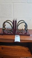 Pair of brass ram head bookends side by side showing design and size relative to furniture.