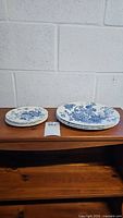 Set of 7 blue and white floral patterned plates, 4 smaller bread and butter plates and 3 larger dinner plates on wooden surface.