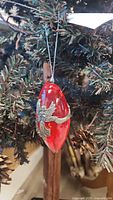 Red glass Christmas ornament with pewter seagull décor hanging on tree branch