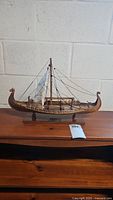 Full view of the vintage wooden Drakkar Viking boat model on a wooden surface showing the dragon-head prow and sail.