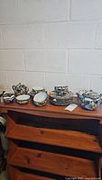 Full view of the entire dish set arranged on wooden shelves showing plates, cups, saucers, teapot, creamer, and sugar bowl