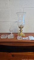 Full view of Waterford crystal hurricane candleholder with brass base surrounded by crystal trinkets and trays on a wooden surface against a white wall.
