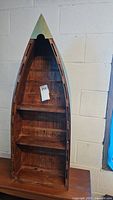 Front view of wooden canoe-shaped shelf showing overall shape and three shelves inside.