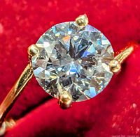 Close-up view of round brilliant cut diamond held by four yellow gold prongs against red background