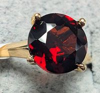 Close-up view of round red garnet in four-prong 10K yellow gold setting