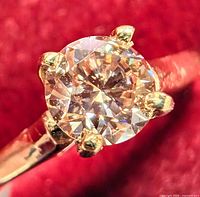 Macro front view of round pink diamond in 4-prong yellow gold setting on red velvet background.