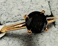Close-up of ring front on grey surface showing round black diamond and prong setting