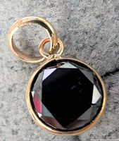 Close-up photo of front side of round faceted black diamond set in 10K yellow gold with circular bail