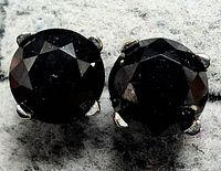 Two black round brilliant cut diamonds set in rhodium-plated 14K white gold prong settings on gray textile background