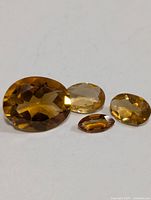 Four loose citrine gemstones arranged in a row showing their size and color differences on white background.