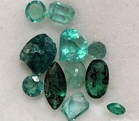 Loose genuine emerald gemstones arranged on white background showing various cuts, colors and sizes.