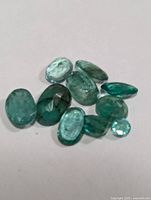 Photo of nine loose emerald gemstones on white background showing their shape and color