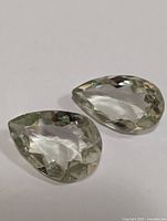 Two green amethyst pear shaped faceted gemstones on white background.