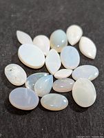 Multiple genuine opal gemstones of mixed shapes on a dark background showing their milky and iridescent characteristics.