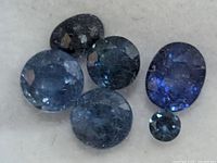 Close-up photo showing five genuine faceted sapphire gemstones in different cuts and shades of blue.