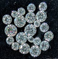 Close-up image of multiple loose round lab grown diamonds on black surface showing size and cut details.