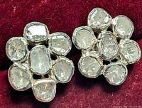 Close-up of one pair of silver earrings with seven natural diamonds each, arranged in a flower cluster shape, on a burgundy velvet background.