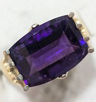 Close-up photograph of cushion-cut amethyst set with six prongs in a silver ring.