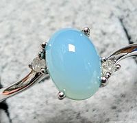 Close-up front angled shot showing oval light blue chalcedony cabochon and two small diamonds on a sterling silver band.