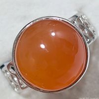 Close up front view of silver band ring with large polished round orange coralian gemstone.