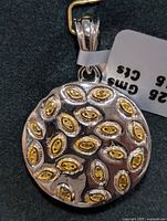 Front view of round silver pendant with gold-toned oval shapes and embedded diamonds, showing pendant bail with price tag.