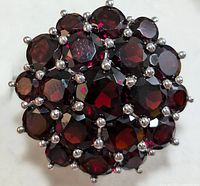 Close-up front view of silver ring with many faceted garnet stones arranged in floral cluster.