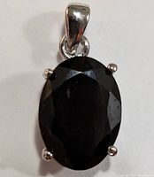 Front view of the oval faceted dark red garnet set in silver with four prongs and a polished bail.