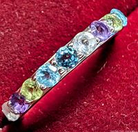 Close-up photo of the sterling silver ring featuring multiple colorful round-cut gemstones on a red fabric background