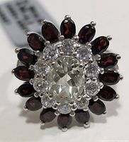 Close-up top view showing oval green amethyst center, surrounded by white stones and garnet stones.