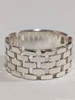 Front view of the silver ring highlighting the woven rectangular block design and open adjustable band.