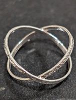 Close-up view of silver ring with intersecting bands and textured detailing on a dark background.
