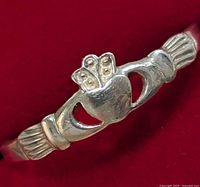 Close-up photo of a silver ring showing the Claddagh design with heart, crown, and hands on red background.