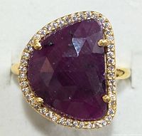 Top front angled close-up view of ring showing large faceted ruby surrounded by small cubic zirconia halo.