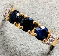 Close-up front view of the silver ring with three round blue sapphires and diamond accents on a grey fabric background.