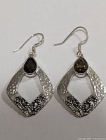 Pair of silver earrings with teardrop smokey quartz and hammered silver open diamond shaped design with ornamental detail.