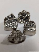 Photo of the four sterling silver Pandora charms arranged on a white surface including a picnic basket, football player, wrapped baby, and pair of bells.