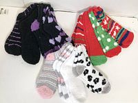 Twelve pairs of winter socks in mixed colors and patterns, laid out on a white surface, including black and purple, white and gray, and red and green color schemes.