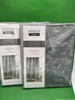 Photo of two unopened packages of Famous Home branded shower curtains, model Etched Rose, showing size and packaging details along with the visible etched rose pattern.