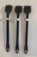 Set of three identical 18-inch long handle BBQ grill brushes with black plastic handles and metal bristles laid side by side against a white background.