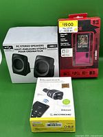 Photo shows three boxed electronics: Crossfade 375 Series 8GB pink MP3 player, PC USB stereo speakers, and Scosche hands-free car kit with Bluetooth and FM transmitter.