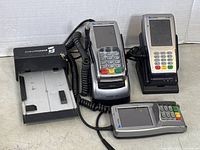 Photo showing three VeriFone payment terminals alongside a manual credit card imprint machine, all placed on neutral background.