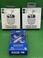 Front view of two white wireless earbuds in rectangular charging cases and one blue box with purple Onn wireless earphones.