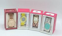 Four wristwatches in individual pink and white boxes, showing different styles and colors.